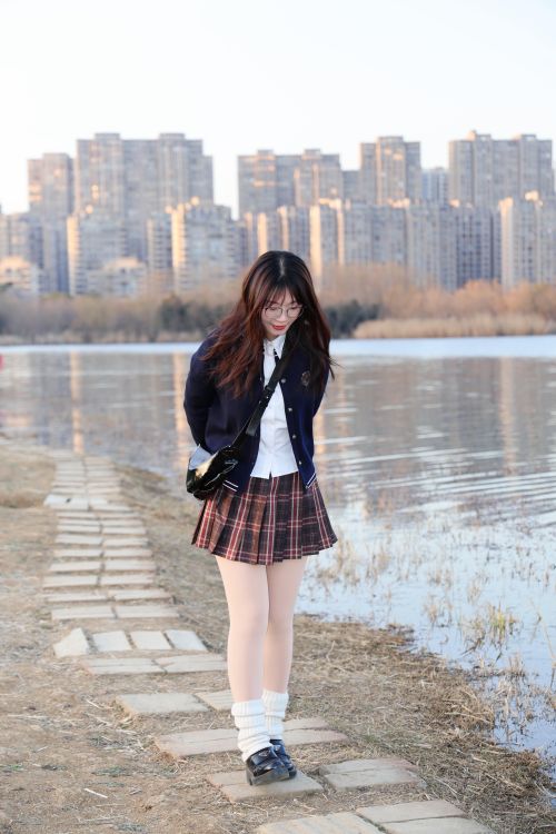Free A young woman strolls by a riverside path in Hefei, China, with a cityscape in the background. Stock Photo