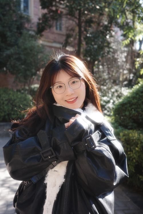 Free A young woman smiling in an outdoor setting in Hefei, China, wearing a black jacket with greenery around. Stock Photo