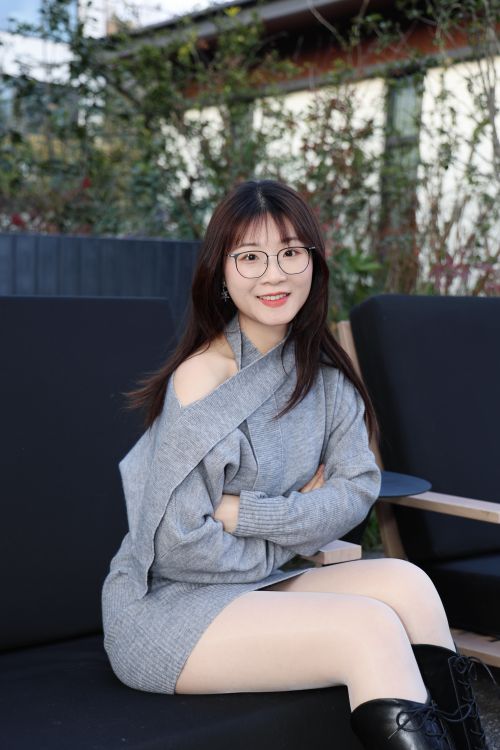 Free Portrait of a young woman seated outdoors wearing a gray sweater with a smile. Stock Photo