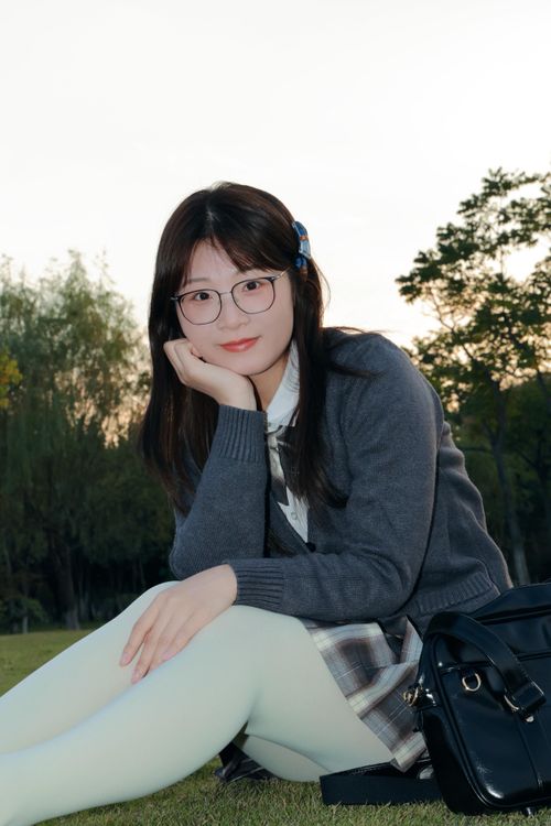 Free A young woman with glasses sits on grass in Hefei park during sunset, showcasing a serene outdoor moment. Stock Photo