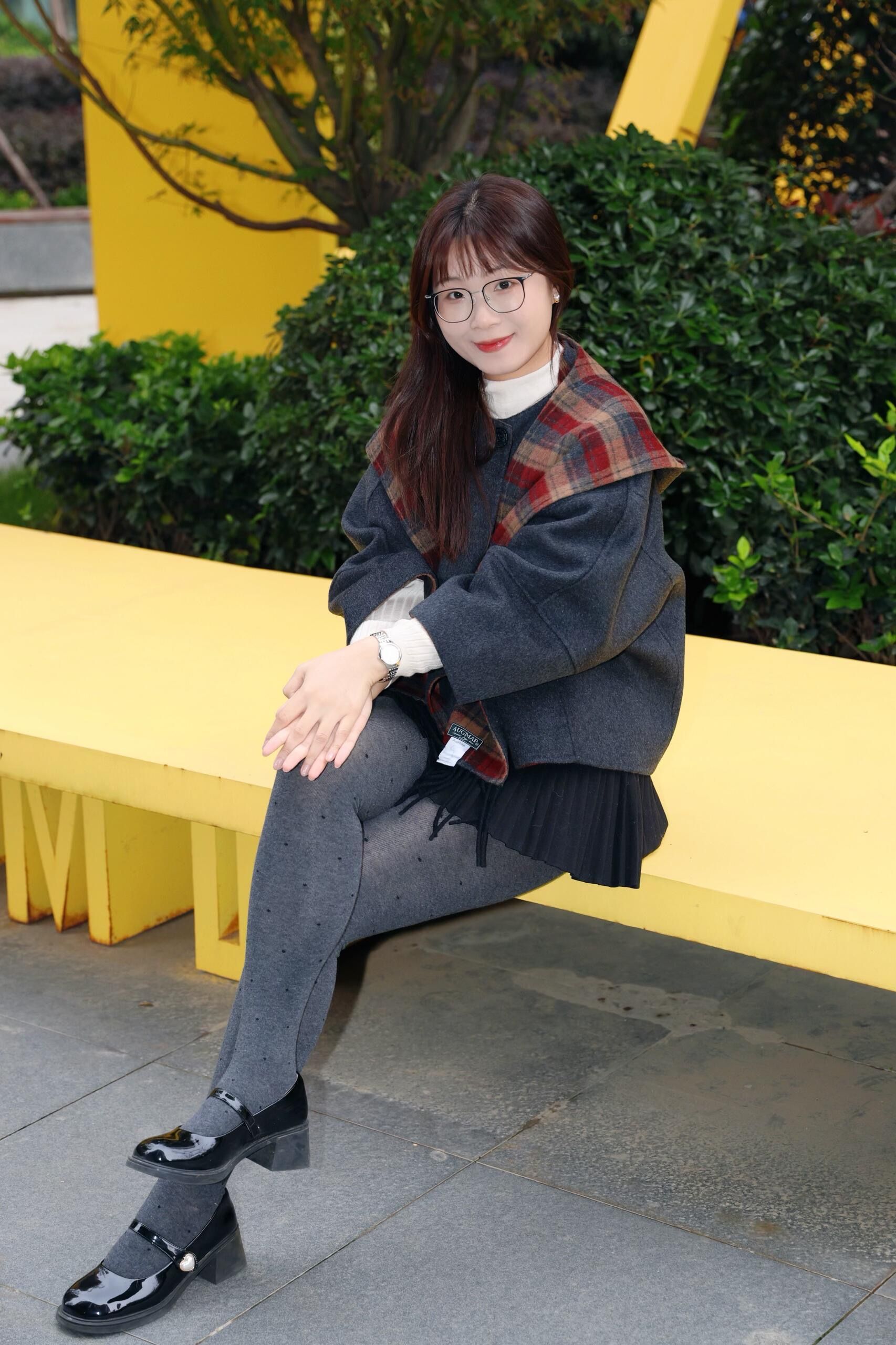 Stylish woman in gray and plaid outfit seated on a yellow bench in Hefei, Anhui, China.