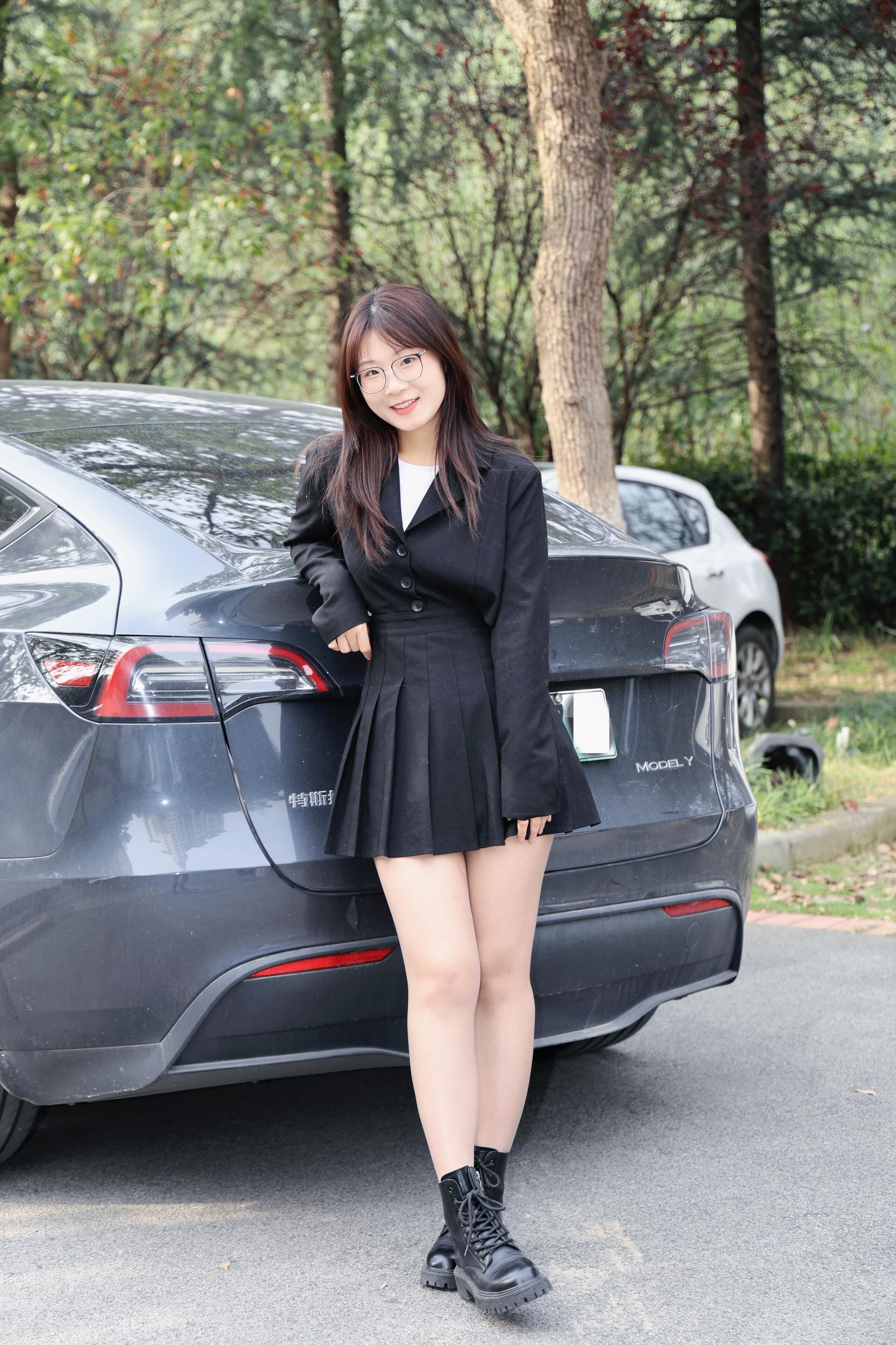 Young woman in stylish black attire posing next to a car outdoors in Hefei, China.