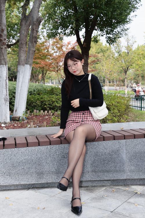 Free A young woman sits on a bench in a Hefei park during fall, wearing stylish autumn attire. Stock Photo