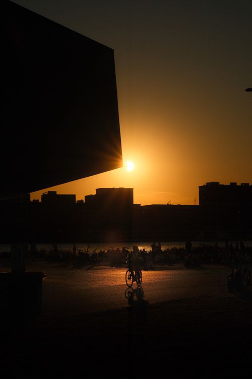 Free Silhouetted cityscape at sunset with cyclists riding along the waterfront. Stock Photo