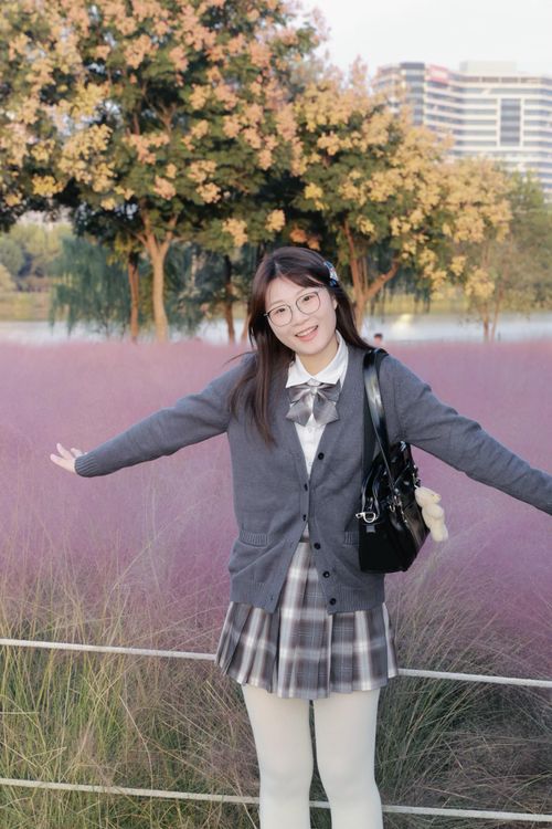 Free A young woman with glasses smiles in an autumn park in Hefei, China, surrounded by pink muhly grass and trees. Stock Photo