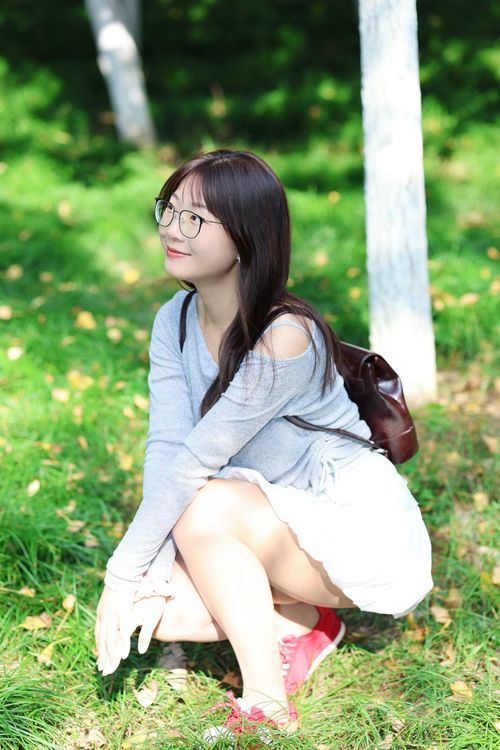 Free Young woman sitting in a sunny park in Hefei, wearing casual clothes and glasses. Stock Photo