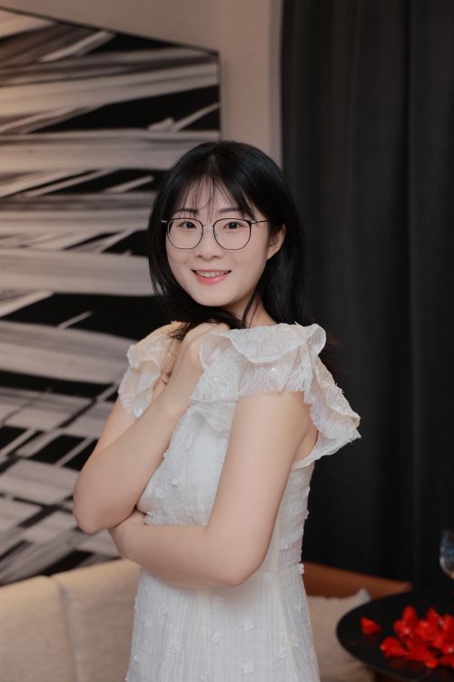 Free A young Asian woman in a white dress poses elegantly indoors with a modern art backdrop, conveying grace and style. Stock Photo