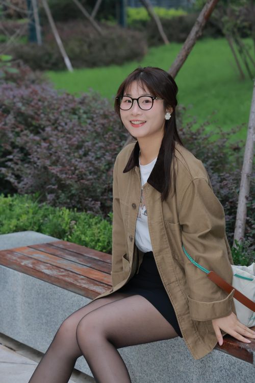 Free A young woman with glasses, seated on a park bench in Hefei, China, enjoying a peaceful day outdoors. Stock Photo