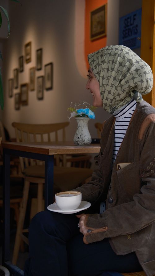 Free A young woman with a headscarf enjoys a cup of coffee in a cozy indoor cafe setting. Stock Photo