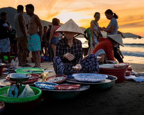 Free People engage in lively trade at a vibrant beach market during sunrise. Stock Photo