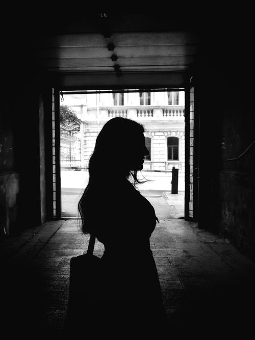 Free Dramatic silhouette of a woman standing in an arched walkway with historic architecture in view. Stock Photo