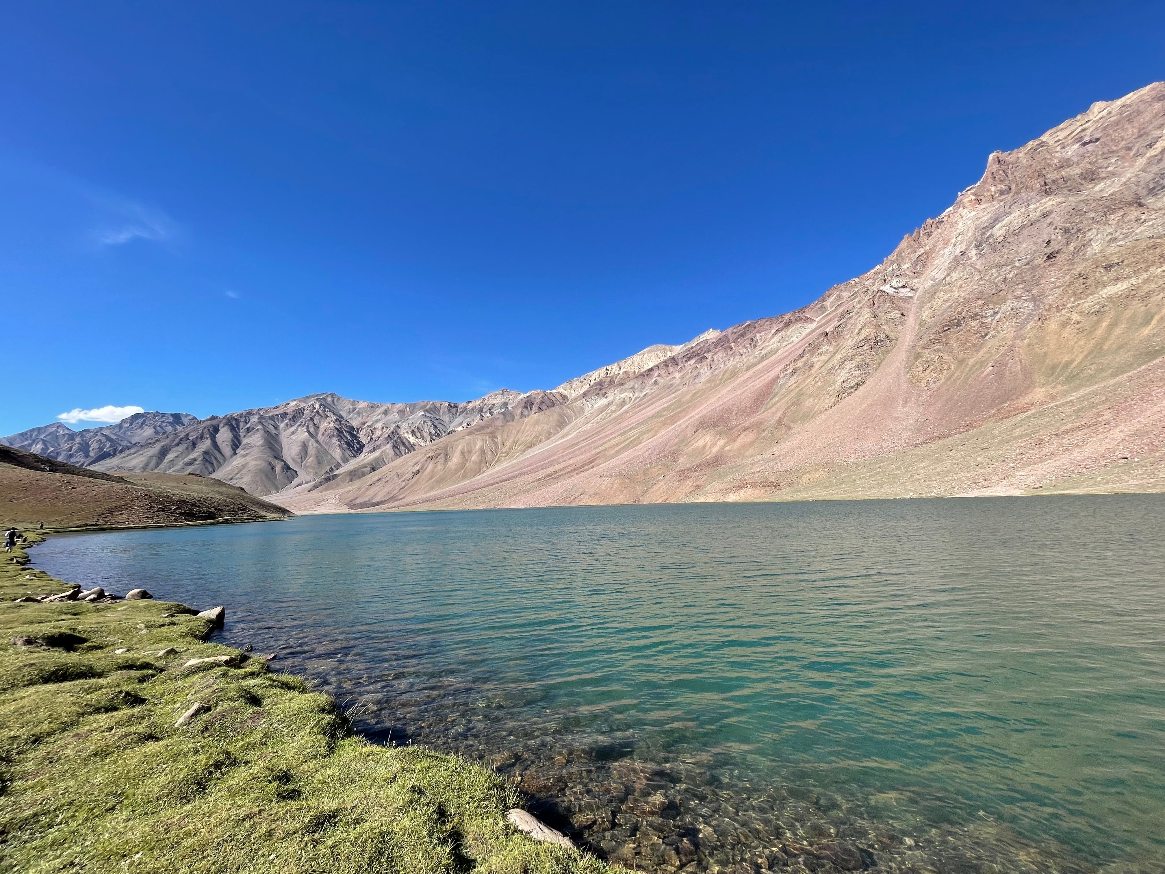 Breathtaking view of Chandra Taal Lake surrounded by majestic Himalayan peaks under a clear blue sky.