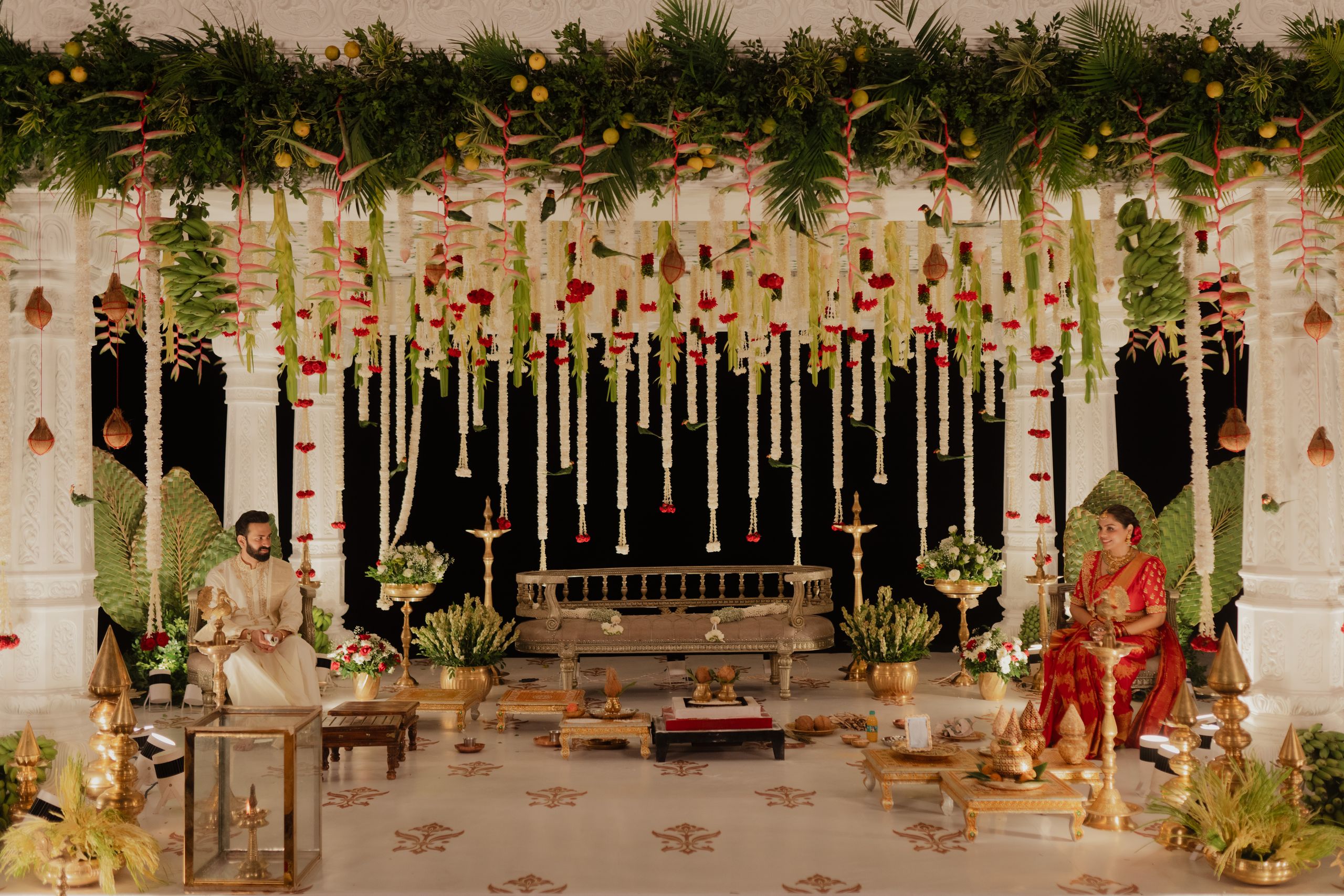 Mandap dressed with cascading strands of white and red flowers, with the couple seated for the ceremony