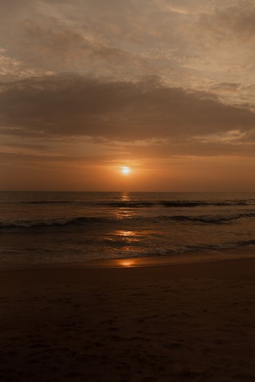 Free Peaceful sunset over a tranquil beach with gentle waves and dramatic clouds. Stock Photo