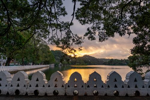 Free A picturesque view of a sunset over Kandy Lake with lush greenery and traditional architecture in the background. Stock Photo