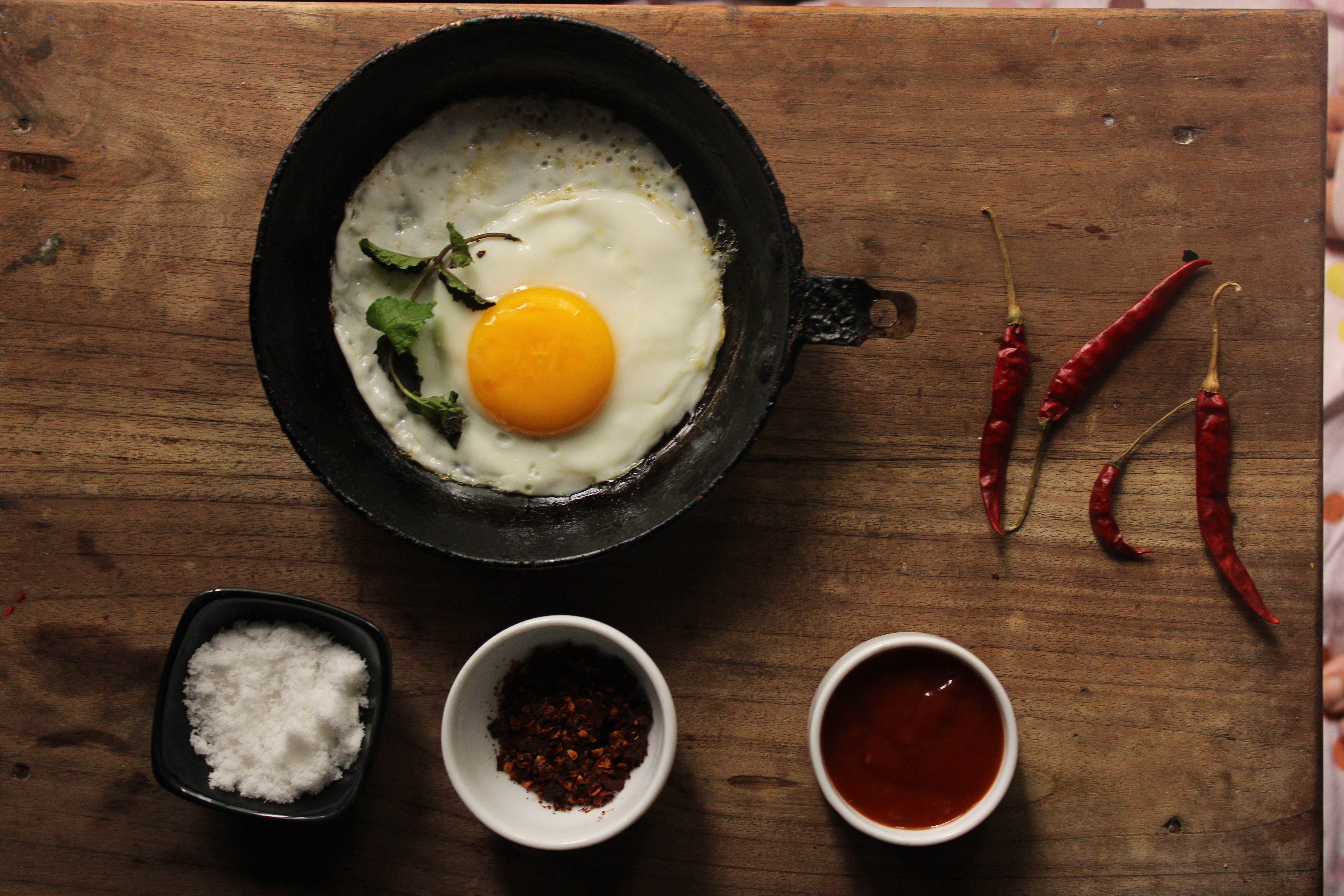 A fried egg in a skillet with spices and red chili peppers on a wooden table. - Photo by Jahra Tasfia Reza on Pexels