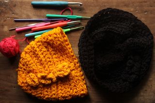 Vibrant crochet beanies with yarn and hooks on wooden table. Perfect for crafts.