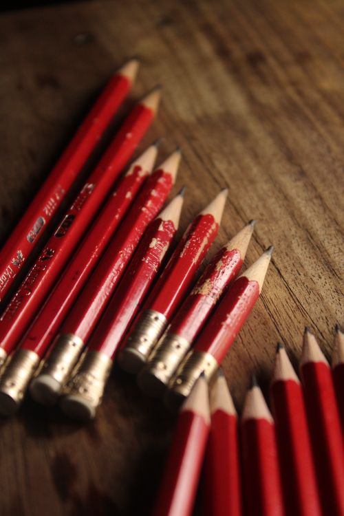 Free A collection of red pencils neatly arranged on a rustic wooden table, offering a warm artistic vibe. Stock Photo