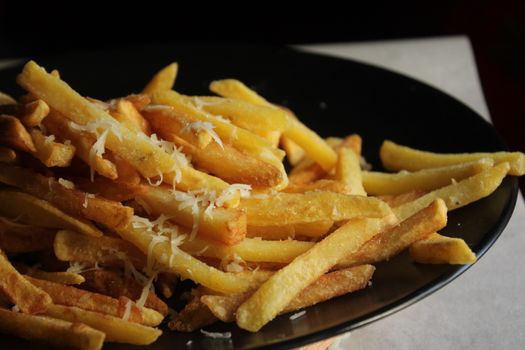 Delicious golden french fries topped with grated cheese on a dark plate.