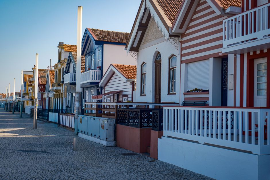 Charming row of colorful striped beach houses under clear blue skies in Costa Nova.