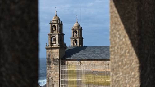 Free View of a historic church's twin bell towers seen through an archway with ocean backdrop. Stock Photo