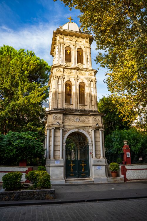 Free A beautifully designed historic bell tower surrounded by lush greenery and soft sunlight. Stock Photo