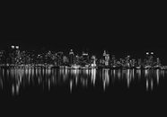 纽约市的天际线在夜间倒映于水面，呈现出迷人的黑白景观