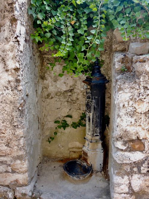 Free A weathered antique water fountain nestled in a rustic stone corner with lush green ivy overhead. Stock Photo