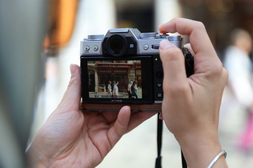 Free Close-up of hands holding a camera capturing a street scene in the display. Stock Photo