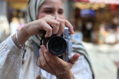 Free A woman with a headscarf photographs her surroundings with a vintage camera on a lively street. Stock Photo