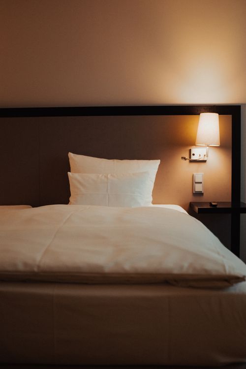 Free A cozy hotel room with a neatly made bed and warm bedside lighting. Stock Photo