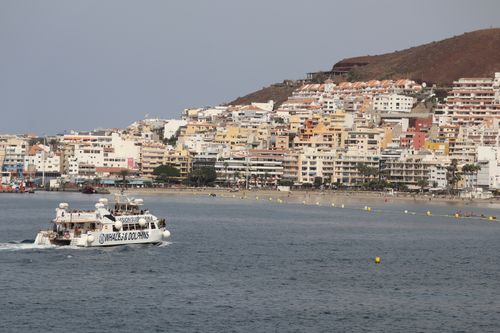 Free Scenic view of a coastal city in Spain with a whale watching boat near the shore. Stock Photo
