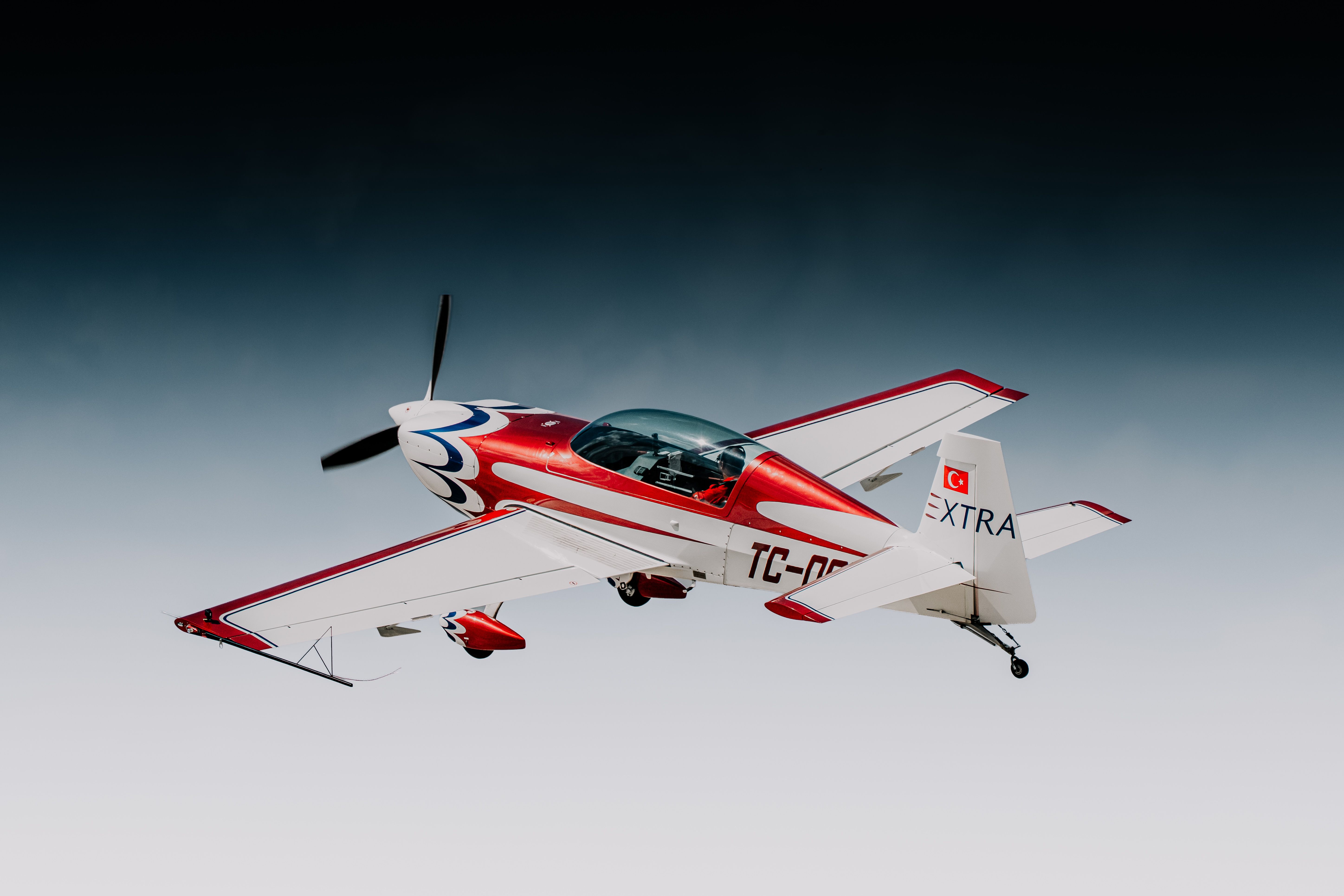 A red and white aerobatic aircraft soaring against a dramatic sky, showcasing agility and performance.