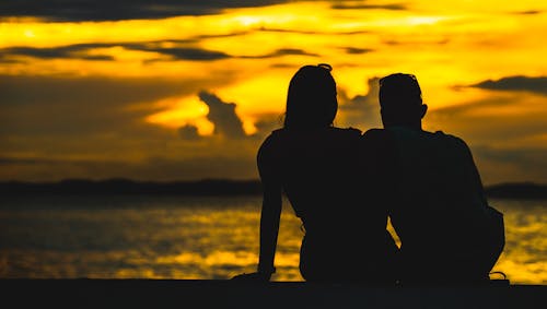Silhouette of Couple Sitting on Seashore during Sunset