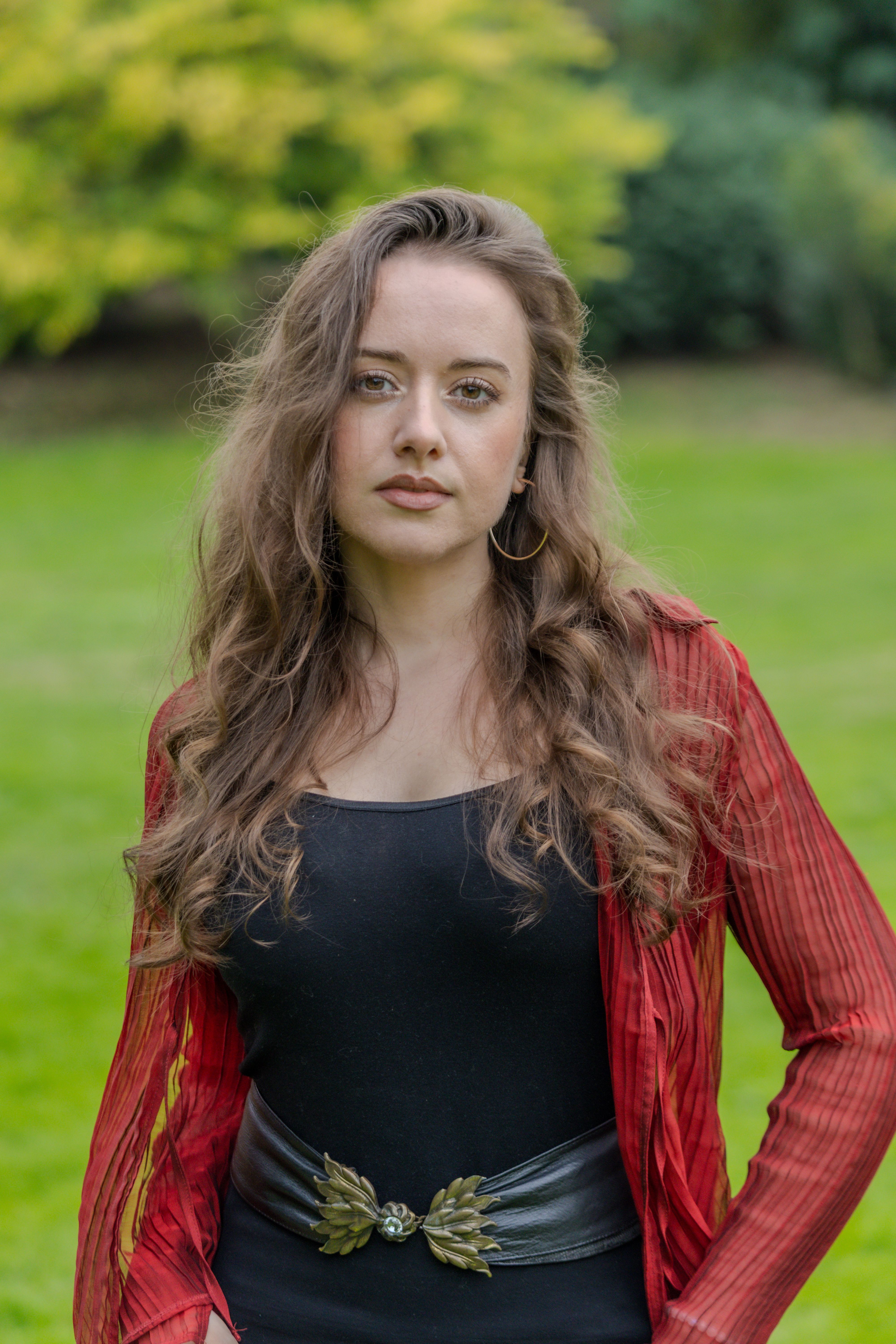 Portrait of a woman in red and black attire standing in a lush green park in Düsseldorf.