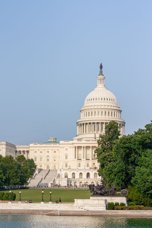 Free The iconic United States Capitol in Washington D.C. under a clear blue sky, surrounded by lush greenery. Stock Photo