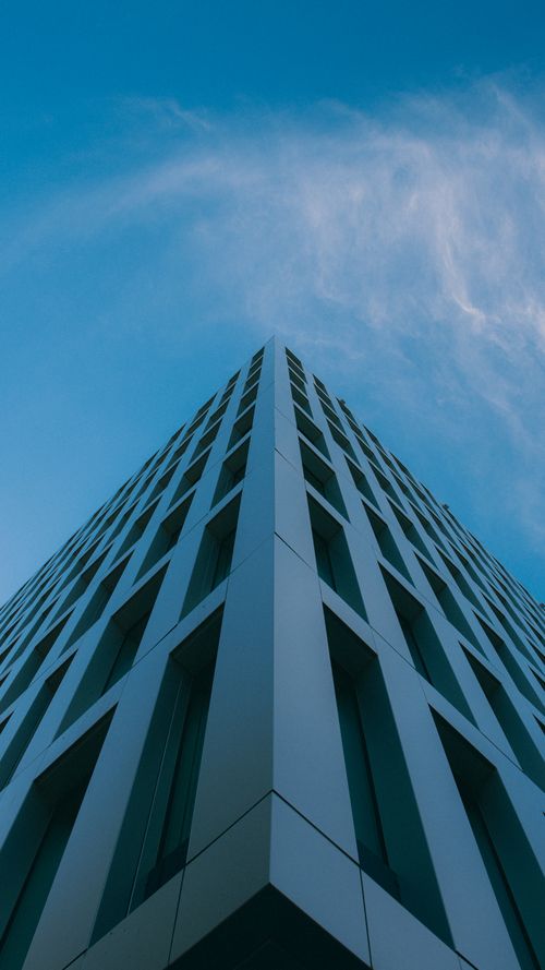 Free Low-angle view of a modern high-rise building with geometric design set against a clear blue sky. Stock Photo