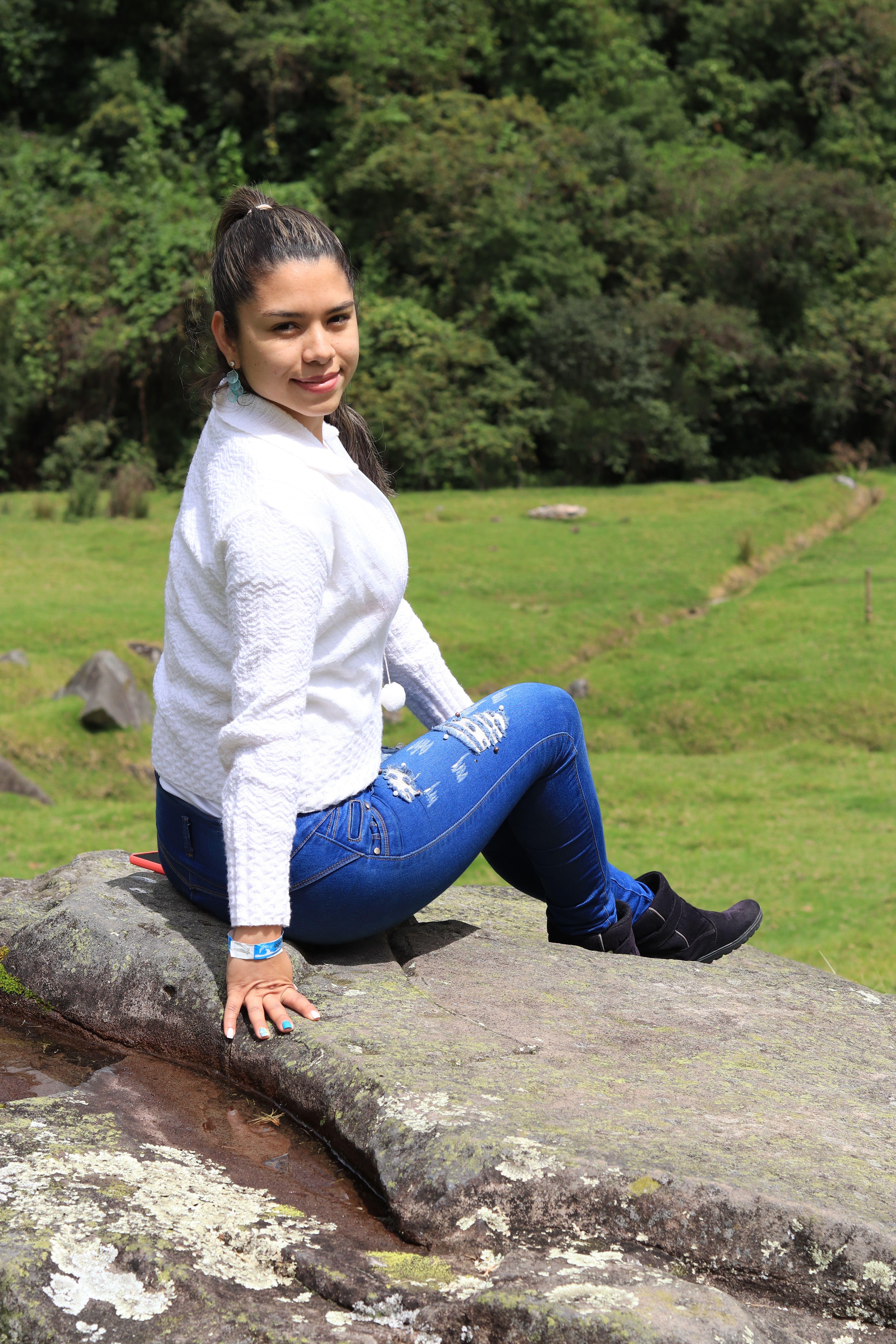 Smiling young woman sitting on a rock in green landscape of Puracé, Colombia.