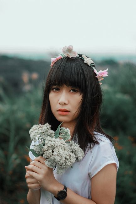 Graceful woman with flower crown holds bouquet, exuding natural beauty.
