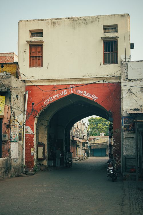 Free Historic red archway in Moga, Punjab, India, leading to a bustling street market. Stock Photo