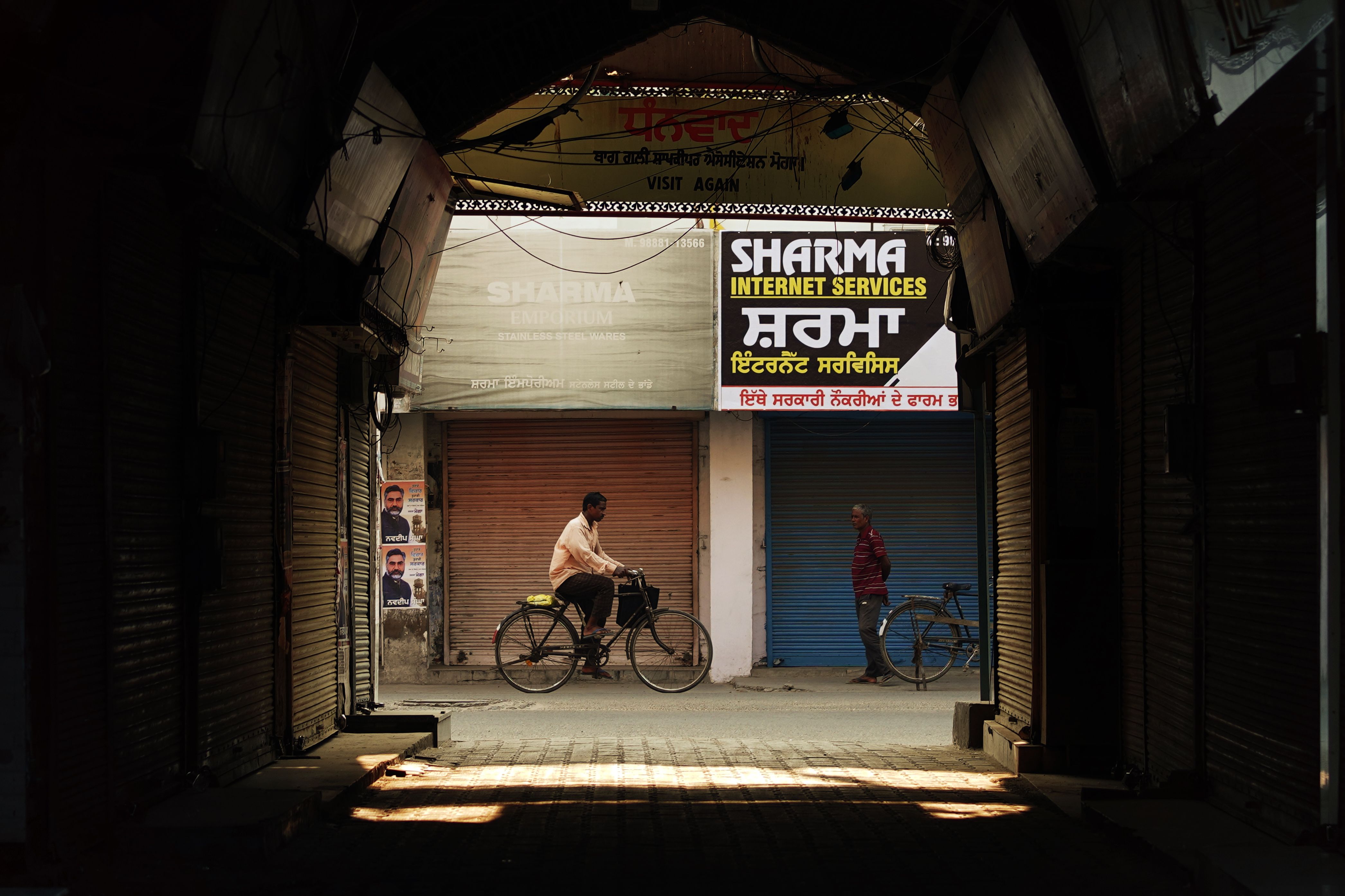 A man on a cycle passes through an archway in Moga, Punjab, with vintage shops lining the street.