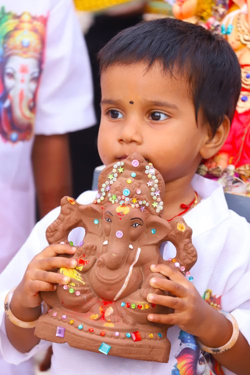 Free Young child holding a decorated clay Ganesh idol during a festive celebration. Stock Photo
