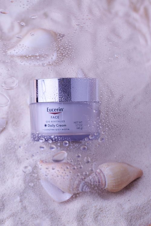 Free High-quality Eucerin face cream jar styled on sand with seashells, highlighting skincare luxury. Stock Photo