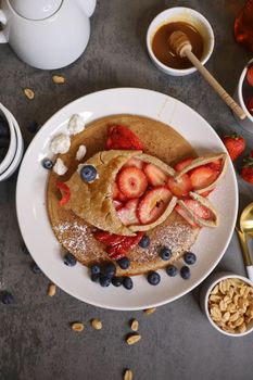 Delicious pancakes topped with fresh strawberries and blueberries, served with honey.