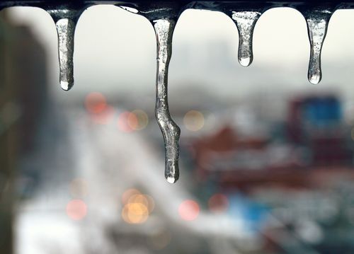 Free Focused icicles hang against a blurred winter cityscape with bokeh lights, capturing a serene winter atmosphere. Stock Photo
