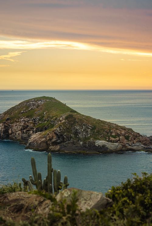 Free Stunning sunset view of a rocky island in Arraial do Cabo, Brazil, with the ocean and cacti in the foreground. Stock Photo