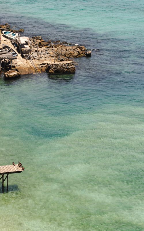 Free Peaceful coastal scene featuring a rocky shoreline, clear water, and a small pier. Stock Photo