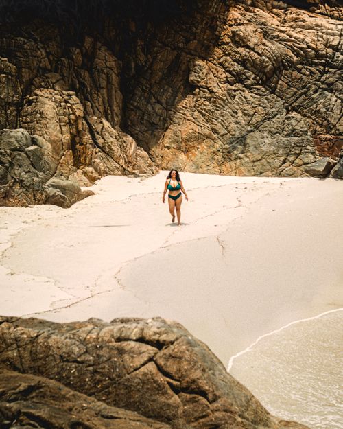 Free A person walks on a secluded beach surrounded by dramatic rocky cliffs, under clear skies. Stock Photo