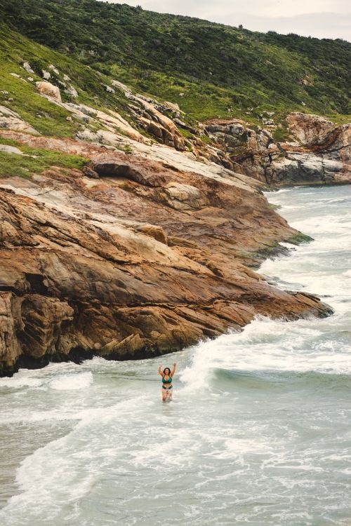 Free A lone swimmer enjoys the waves along a rocky coastline, capturing a serene beach scene. Stock Photo