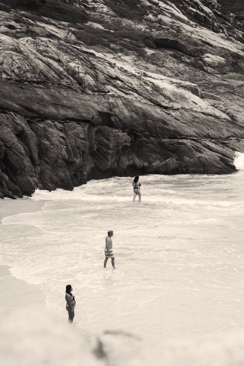 Free Three people enjoying a peaceful day by the rocky shores of Arraial do Cabo. Stock Photo